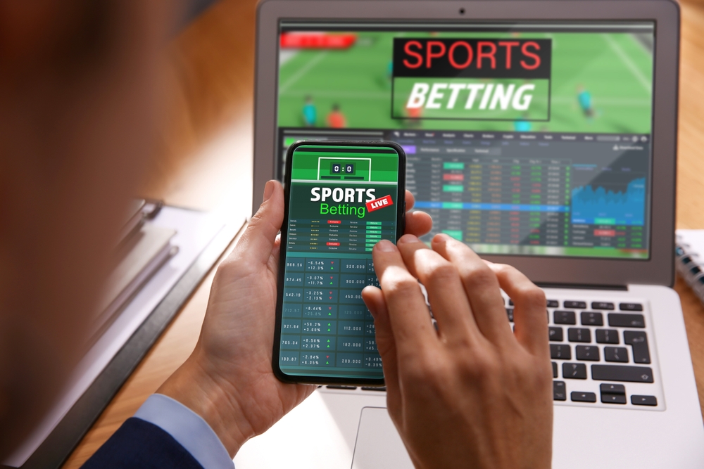 Man,Betting,On,Sports,Using,Smartphone,And,Laptop,At,Table,